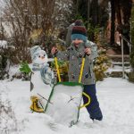 Dječak istovarlja snijeg iz Rolly Toys John Deere tački